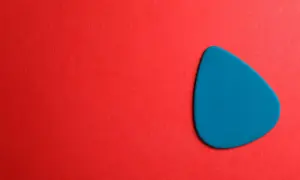 Ein blaues Plektrum liegt auf rotem Untergrund. Was ist ein Plektrum? Ein kleines Werkzeug zum Zupfen von Saiten.