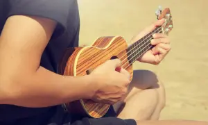 Person spielt auf einer Ukulele, die Hände formen den D-Dur-Akkord. Die Holzmuster der Ukulele sind gut sichtbar.