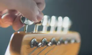 Eine Hand dreht an einer Mechanik des **Gitarrenkopfes**, um die Saiten zu stimmen.