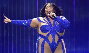 Sängerin in blauem Glitzer-Outfit singt mit Mikrofon, die Arme ausgestreckt. Ein Auftritt, der nach dem besten Lied klingt.
