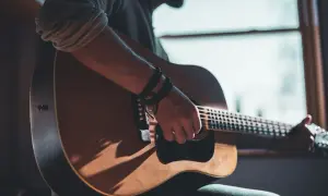 Mann spielt Akustikgitarre, Schatten fallen auf das Holz. Informiere dich über die Gitarrenunterricht Kosten, um deine musikalischen Träume zu verwirklichen.