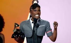 Glückliche schwarze Rapperin mit Grammy-Trophäe und einzigartiger Frisur, die auf der Bühne jubelt.
