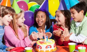 Kinder mit bunten Partyhüten singen Geburtstagslieder für ein Mädchen mit einem Kuchen.