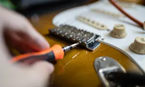Hand mit Schraubendreher stellt die Gitarre ein.