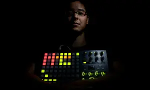 Mann hält leuchtendes Akai APC 40 MK2. Bunte Pads und Regler erhellen die Dunkelheit.