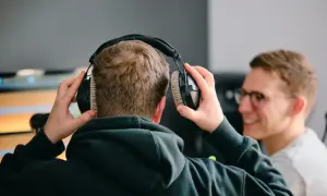 Zwei Männer bereiten sich darauf vor, einen Podcast aufzunehmen. Einer setzt sich Kopfhörer auf, während der andere lächelnd zusieht.