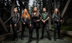 Fünf Musiker in Lederjacken, die an Metal Bands der 80er erinnern, posieren vor einer Holzkonstruktion im Wald.