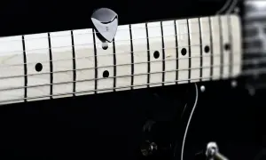 Nahaufnahme eines Plektrums auf den Saiten einer Gitarre. Perfekt, um die **Gitarre Saitenlage einstellen** zu lernen.