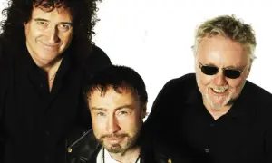Die Queen Mitglieder heute: Brian May, Adam Lambert und Roger Taylor posieren lächelnd in schwarzen Hemden.