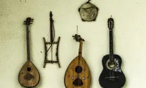 Alte Saiteninstrumente hängen an der Wand. Eine schwarze Gitarre, eine birnenförmige Laute und zwei weitere, wie sie die erste Gitarre aussehen ließen.