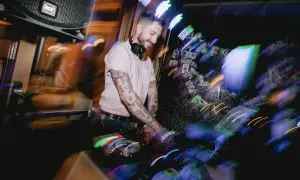 Ein guter DJ mit tätowierten Armen legt Musik auf, während bunte Lichter die Szene in Bewegung setzen.