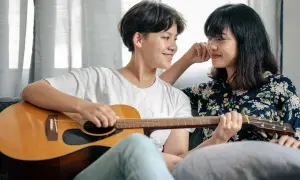 Zwei Frauen auf einer Couch, eine spielt Gitarre, die andere hört zu. Sie scheinen die besten Liebeslieder zu singen.