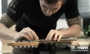 Ein Mann arbeitet an der bund gitarre. Er justiert die Saiten mit seinen Fingern.