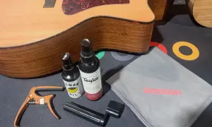Gitarre reinigen: Zubehör wie Saitenwickler, Kapodaster und Pflegeprodukte liegen neben einer Akustikgitarre.