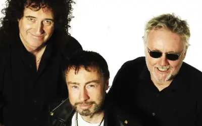 Die Queen Mitglieder heute: Brian May, Adam Lambert und Roger Taylor posieren lächelnd in schwarzen Hemden.