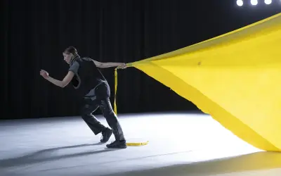Tänzerin zieht ein gelbes Tuch, das sich wie ein Segel im Wind kräuselt. Perfekt für gute Lieder zum Tanzen Choreographie.