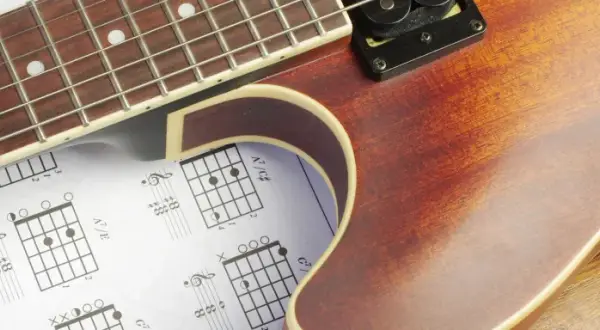 Gitarrenhals über Notenblättern mit Akkorddiagrammen. Perfekt für Gitarre Grundlagen.