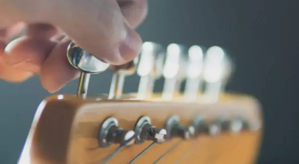 Eine Hand dreht an einer Mechanik des **Gitarrenkopfes**, um die Saiten zu stimmen.