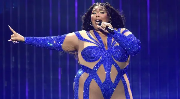 Sängerin in blauem Glitzer-Outfit singt mit Mikrofon, die Arme ausgestreckt. Ein Auftritt, der nach dem besten Lied klingt.