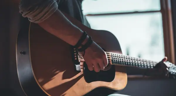 Mann spielt Akustikgitarre, Schatten fallen auf das Holz. Informiere dich über die Gitarrenunterricht Kosten, um deine musikalischen Träume zu verwirklichen.