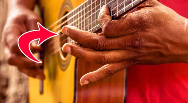 Hände spielen Fingerstyle Gitarre. Ein roter Pfeil zeigt auf die Finger, die die Saiten greifen.