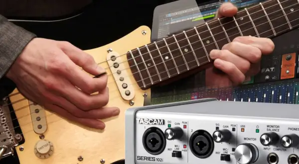 Gitarre aufnehmen PC: Hände spielen Gitarre, daneben ein Audio-Interface und eine DAW-Oberfläche.