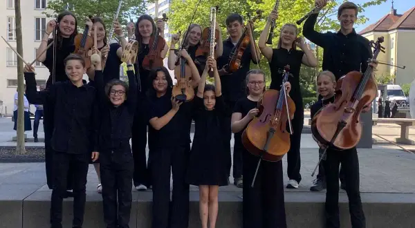 Junge deutsche Bands: Kinder und Jugendliche mit Streichinstrumenten, Flöten und Klarinetten posieren fröhlich für ein Foto.