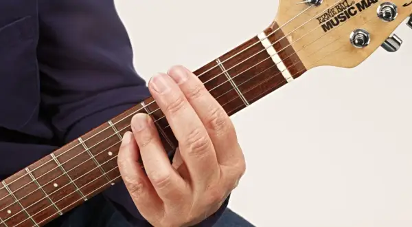 Gitarrenhals mit einem Finger, der einen Barre-Akkord greift. Der Zeigefinger liegt quer über alle Saiten.