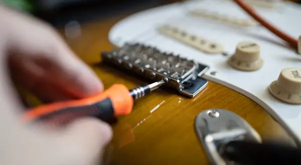 Hand mit Schraubendreher stellt die Gitarre ein.