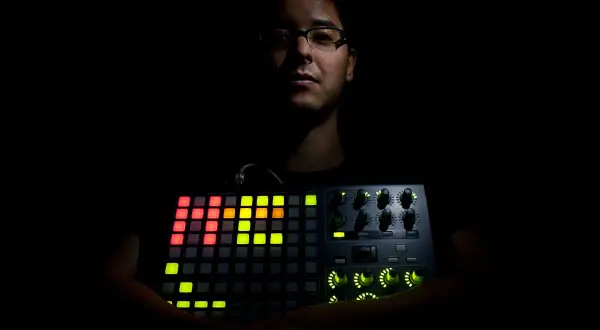 Mann hält leuchtendes Akai APC 40 MK2. Bunte Pads und Regler erhellen die Dunkelheit.