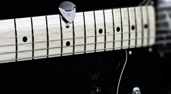 Nahaufnahme eines Plektrums auf den Saiten einer Gitarre. Perfekt, um die **Gitarre Saitenlage einstellen** zu lernen.