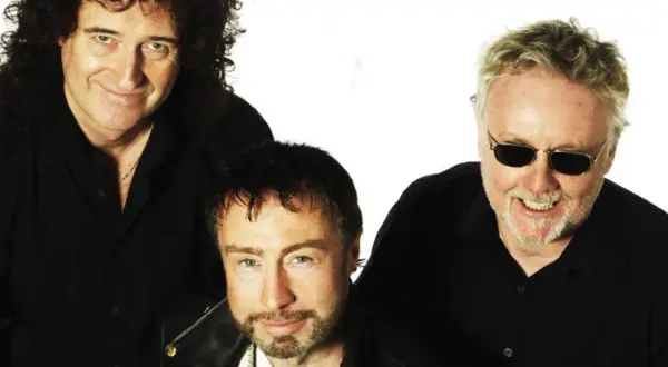 Die Queen Mitglieder heute: Brian May, Adam Lambert und Roger Taylor posieren lächelnd in schwarzen Hemden.