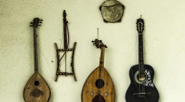 Alte Saiteninstrumente hängen an der Wand. Eine schwarze Gitarre, eine birnenförmige Laute und zwei weitere, wie sie die erste Gitarre aussehen ließen.
