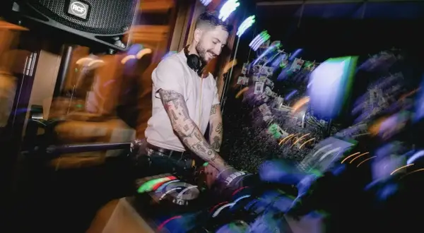 Ein guter DJ mit tätowierten Armen legt Musik auf, während bunte Lichter die Szene in Bewegung setzen.