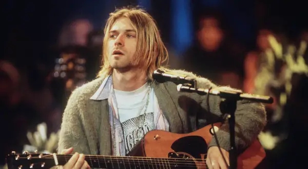 Kurt Cobain spielt Akustikgitarre, ein ikonisches Bild, das an eine verstorbene Rockmusiker Liste erinnert.