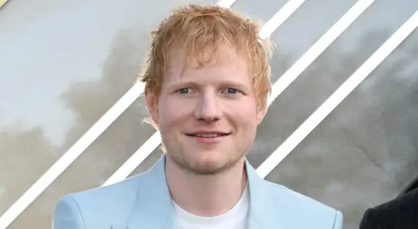 Ed Sheeran, der aus Halifax, England, stammt, lächelt in einem hellblauen Anzug.