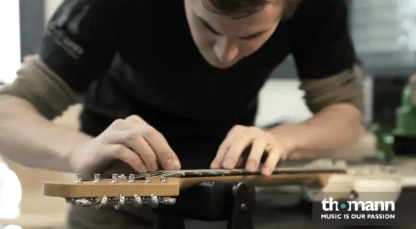 Ein Mann arbeitet an der bund gitarre. Er justiert die Saiten mit seinen Fingern.