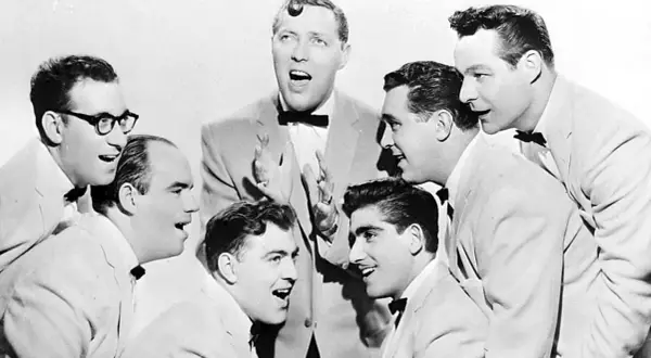 Gruppe von Männern in Anzügen und mit Fliegen, die singen.