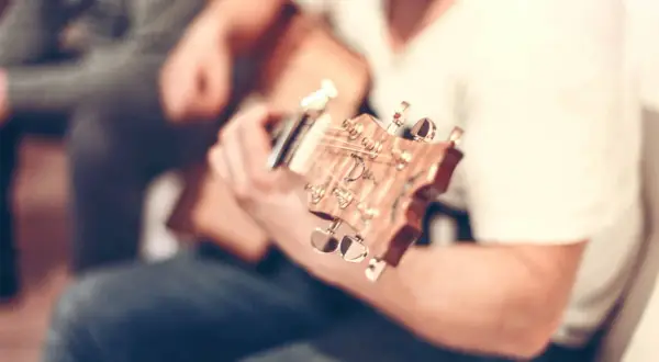 Nahaufnahme einer **bending Gitarre**, die von einer Person gespielt wird. Der Fokus liegt auf dem Hals und den Stimmmechaniken.