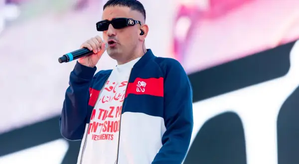 Der beste deutsche Rapper mit Mikrofon auf der Bühne, trägt Sonnenbrille und Bomberjacke.