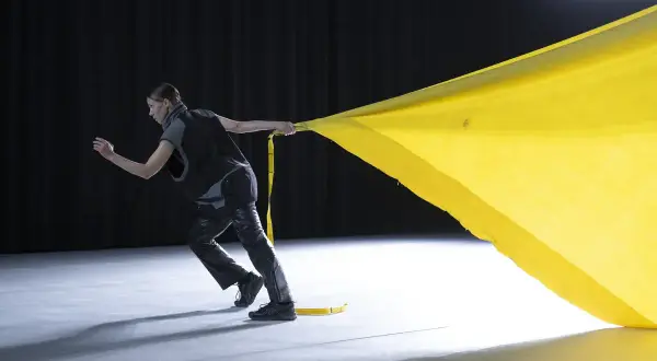 Tänzerin zieht ein gelbes Tuch, das sich wie ein Segel im Wind kräuselt. Perfekt für gute Lieder zum Tanzen Choreographie.
