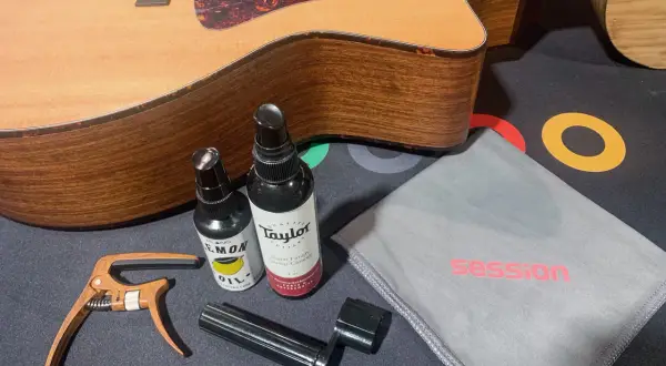 Gitarre reinigen: Zubehör wie Saitenwickler, Kapodaster und Pflegeprodukte liegen neben einer Akustikgitarre.