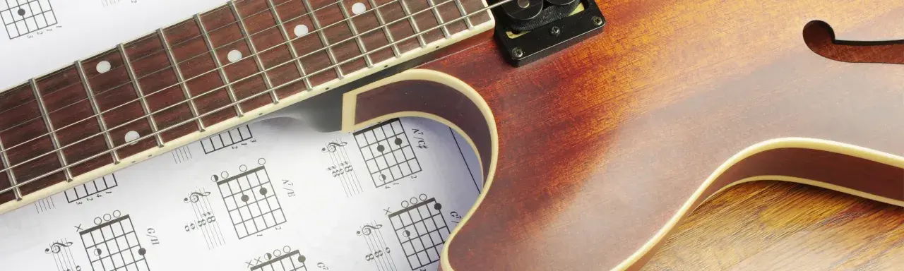 Gitarrenhals über Notenblättern mit Akkorddiagrammen. Perfekt für Gitarre Grundlagen.