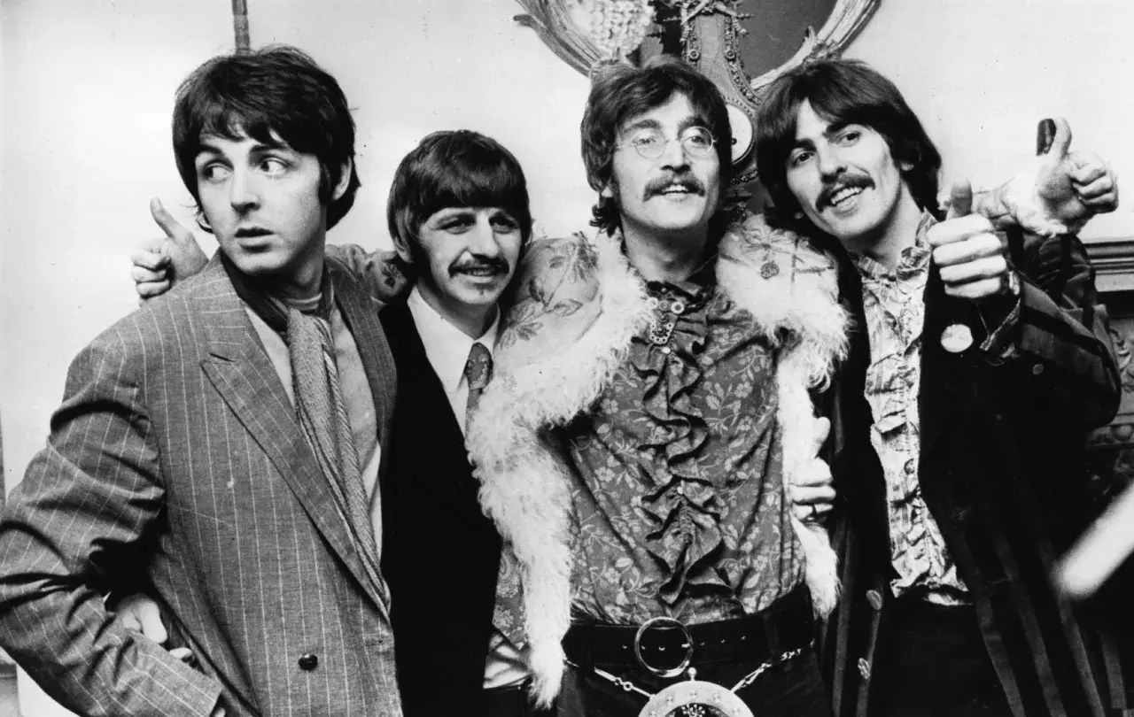 Die Mitglieder von The Beatles, Paul McCartney, Ringo Starr, John Lennon und George Harrison, posieren lächelnd für ein Foto.