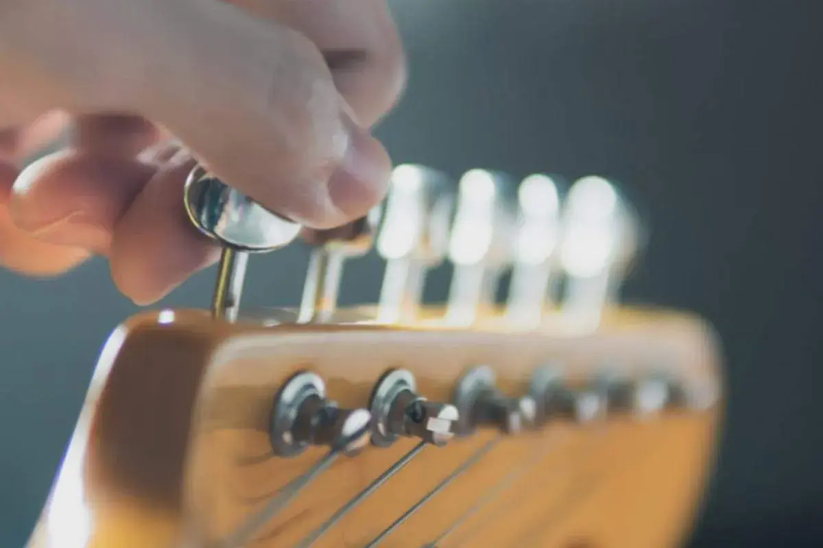Eine Hand dreht an einer Mechanik des **Gitarrenkopfes**, um die Saiten zu stimmen.