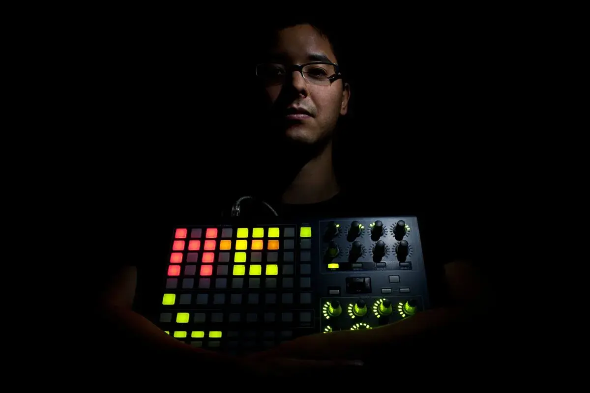 Mann hält leuchtendes Akai APC 40 MK2. Bunte Pads und Regler erhellen die Dunkelheit.