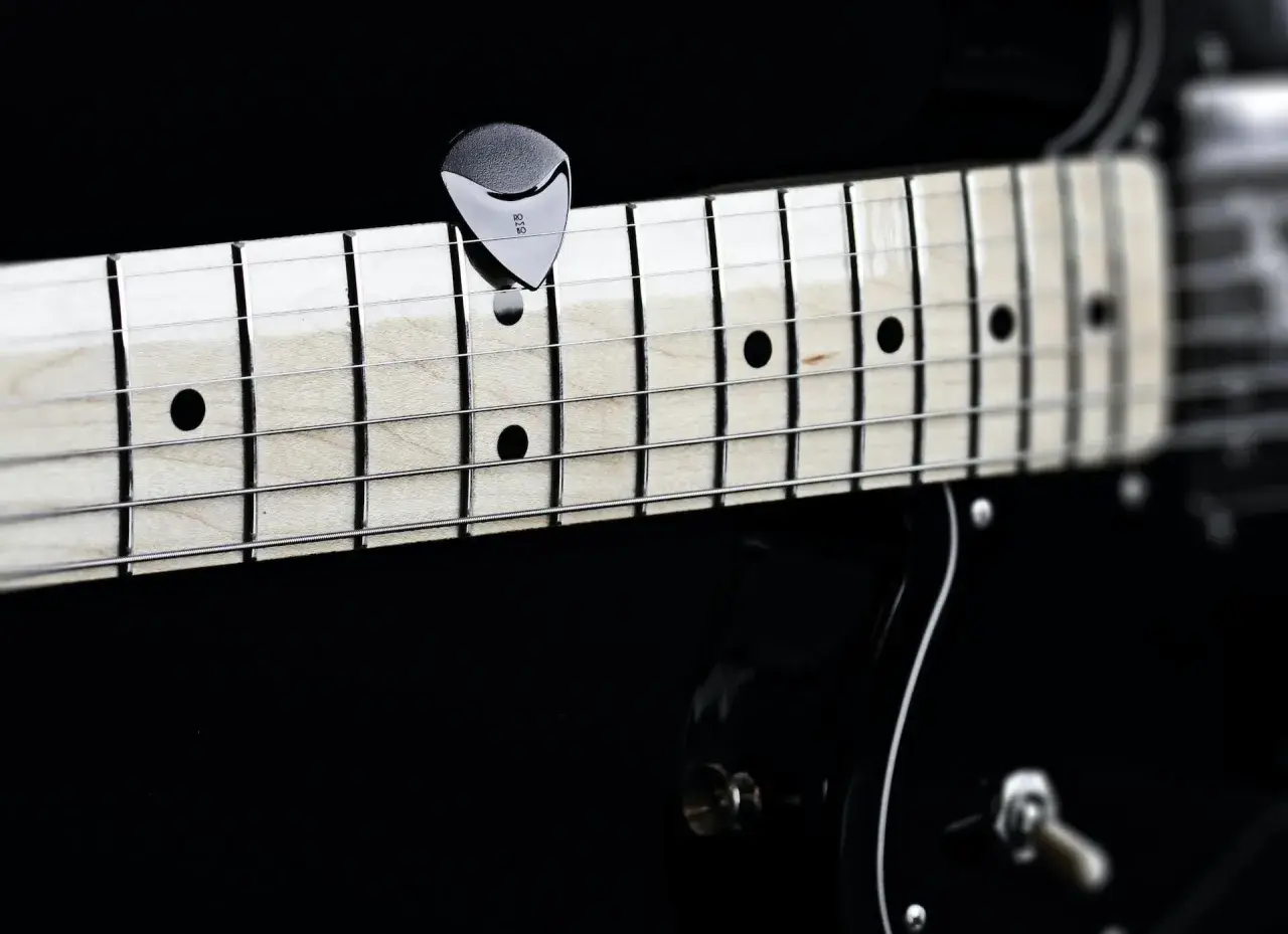 Nahaufnahme eines Plektrums auf den Saiten einer Gitarre. Perfekt, um die **Gitarre Saitenlage einstellen** zu lernen.