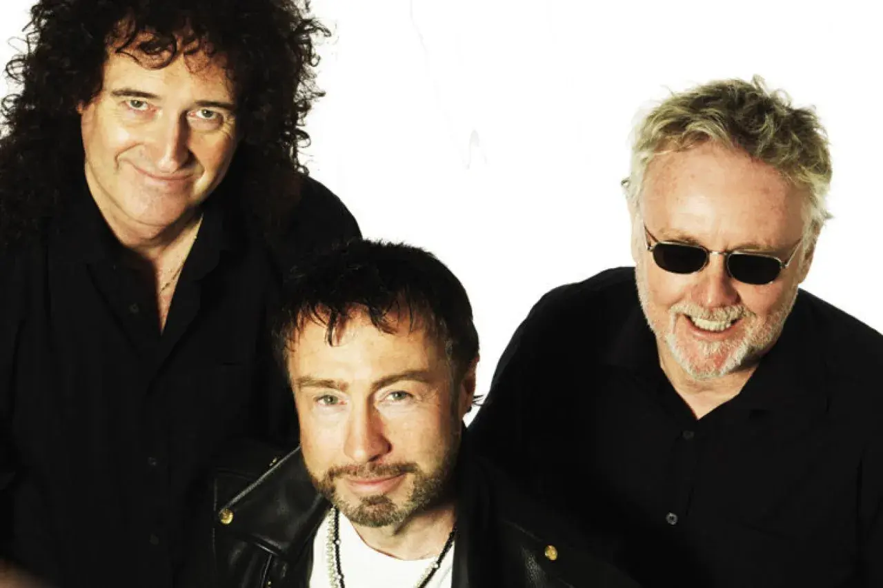 Die Queen Mitglieder heute: Brian May, Adam Lambert und Roger Taylor posieren lächelnd in schwarzen Hemden.
