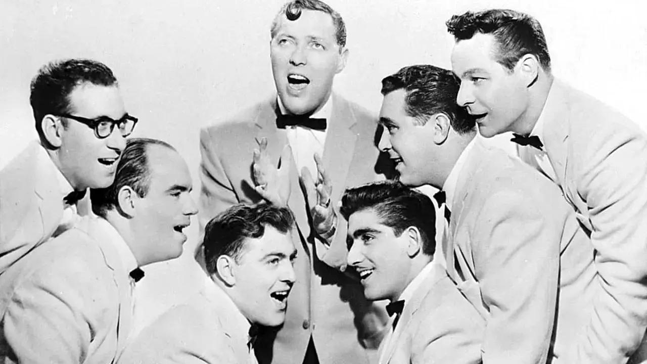Gruppe von Männern in Anzügen und mit Fliegen, die singen.