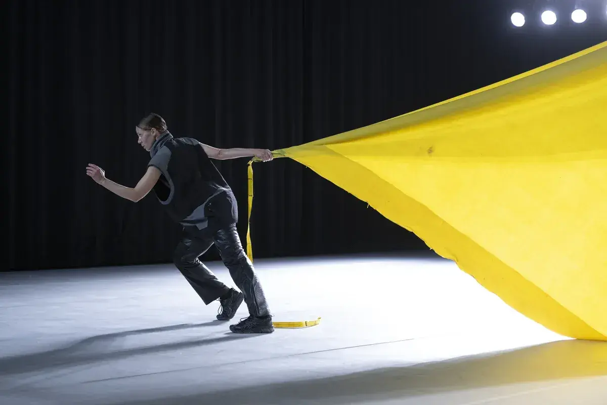Tänzerin zieht ein gelbes Tuch, das sich wie ein Segel im Wind kräuselt. Perfekt für gute Lieder zum Tanzen Choreographie.